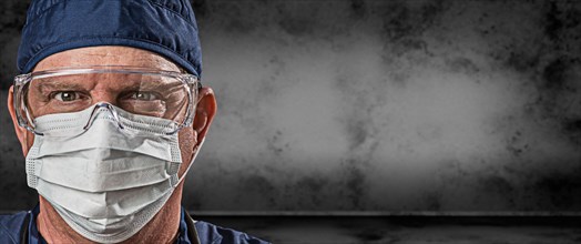 Male doctor or nurse wearing goggles and face mask against grungy dark background banner
