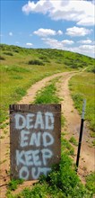 Dead end keep out sign on wire fence at dirt road