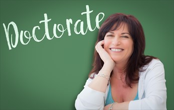 Doctorate written on green chalkboard behind smiling middle aged woman