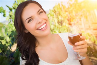 Beautiful young adult woman enjoying glass of wine tasting in the vineyard