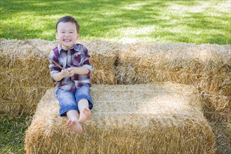 Cute young mixed-race boy having fun on hay bale outside