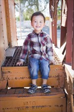 Cute young mixed-race boy having fun outside sitting on railroad car steps
