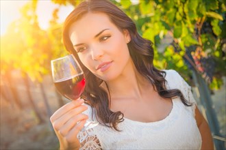 Beautiful young adult woman enjoying glass of wine tasting in the vineyard