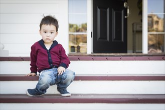 Cute melancholy mixed-race boy sitting on front porch steps