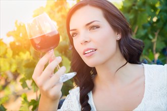 Beautiful young adult woman enjoying glass of wine tasting in the vineyard