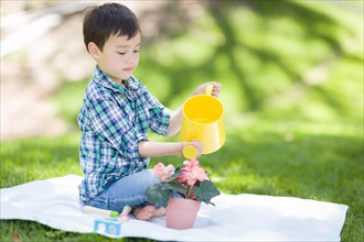 mixed-race young boy watering his potted flowers outside on the grass