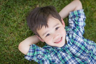 mixed-race chinese and caucasian young boy relaxing on his back outside on the grass