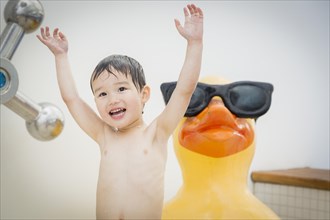 mixed-race boy having fun at the water park with large rubber duck in the background