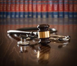 Gavel and stethoscope on wooden table with law books in background