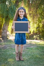 Cute young mixed-race girl holding blank blackboard outdoors
