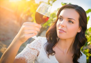 Beautiful young adult woman enjoying glass of wine tasting in the vineyard