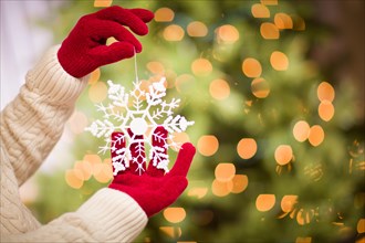 Woman wearing seasonal red mittens holding white snowflake christmas ornament