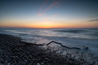 Langzeitbelichtung von einem Ast am Strand der Ostsee bei Sonnenuntergang und starkem Wellengang