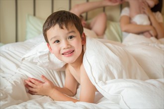 Young mixed-race chinese and caucasian boy laying in bed with thier father and mother