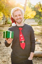 Handsome festive young caucasian man holding christmas gift outdoors