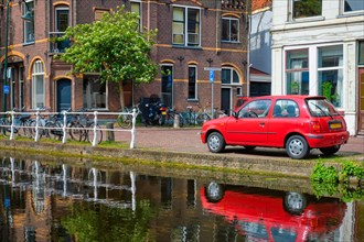 Cars and bicycles on canal embankment in street of Delft with reflection. Delft