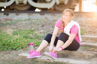 Young adult woman outdoors with towel and water bottle tying her shoe ready for workout