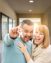 mixed-race couple holding house keys inside hallway of their new home