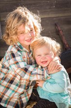 Sweet little boy plays with his baby sister in a rustic ranch setting at the pumpkin patch