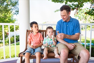 Caucasian father sitting with his mixed-race chinese and caucasian boys enjoying ice cream cones