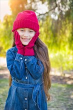 Cute mixed-race young girl wearing red knit cap and mittens outdoors