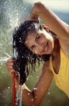Young woman washes her hair with garden hose