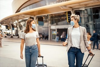 Traveling women in protective masks talking when leaving the airport at their destination