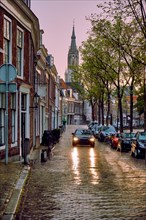 Delft cobblestone street with car in the rain with Nieuwe Kerk church tower in background
