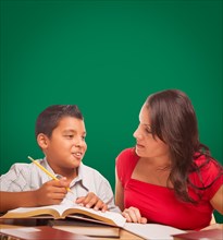 Blank chalk board behind hispanic young boy and famale adult studying