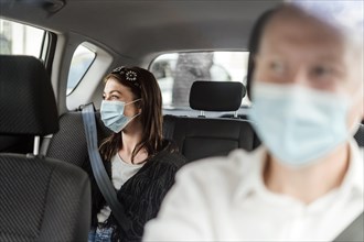 A woman wearing a protective mask sitting on the back seat of a taxi car