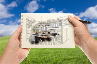 Male hands holding pen and pad of paper up with custom kitchen illustration outside near grass field and blue sky