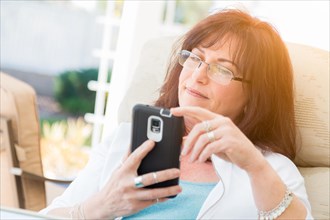 Attractive middle aged woman using her smart phone on the patio