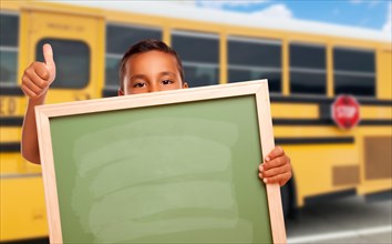 Young hispanic boy with blank chalkboard near school bus