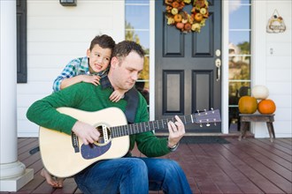 Young mixed-race chinese and caucasian son singing songs and playing guitar with father