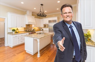 Smiling male agent reaching for hand shake in beautiful new kitchen