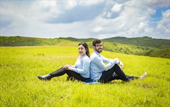 Wedding couple in the field sitting back to back facing the camera
