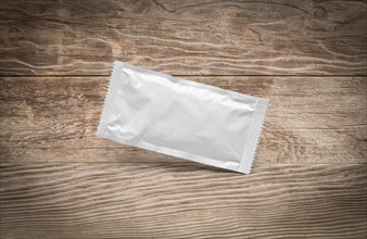 Blank white condiment packet floating on aged wood background