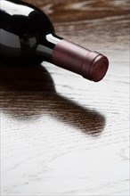 Red wine bottle laying on a wood surface fading down to white