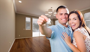 Young military couple with house keys in empty room of new home