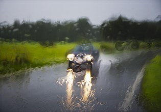Blick durch eine nasse Windschutzscheibe auf ein fahrendes Auto auf einer Strasse bei Regenwetter