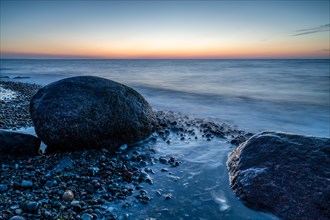 Langzeitbelichtung von grossen Felsbrocken am steinigen Strand der Ostsee bei Sonnenuntergang