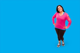 Middle aged hispanic woman in workout clothes against A bright cyan blue background