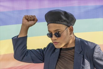 Portrait of a gay latin man with makeup wearing a fashionable hat on a rainbow background