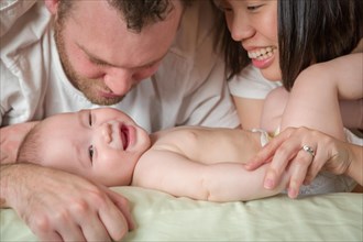 mixed-race chinese and caucasian baby boy laying in bed with his parents