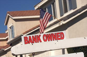 Bank owned real estate sign and house with american flag in the background