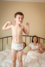 Young mixed-race chinese and caucasian boy jumping in bed with his family