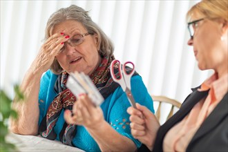 Financial consultant handing scissors to senior lady holding credit cards