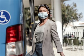 A young woman wearing protective medical mask boarding the bus with a luggage