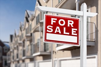 For sale real estate sign in front of a row of apartment condominiums balconies and garage doors