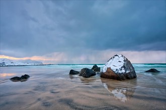 Rocks covered with snow on Norwegian sea beach in fjord in stormy weather with clouds